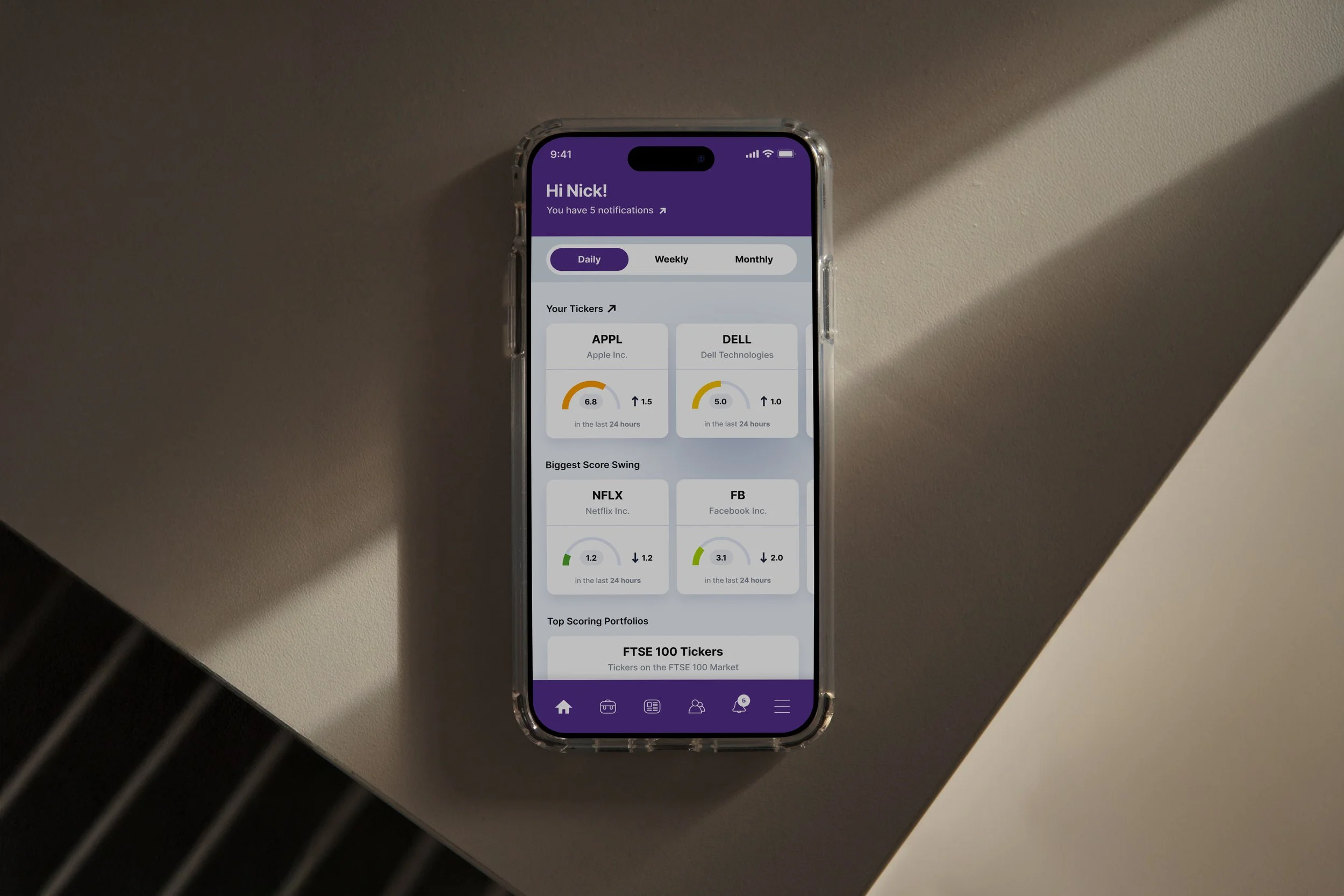 A smartphone on a table displaying a stock market app with stock tickers, scores, and portfolio information on a purple and gray interface.