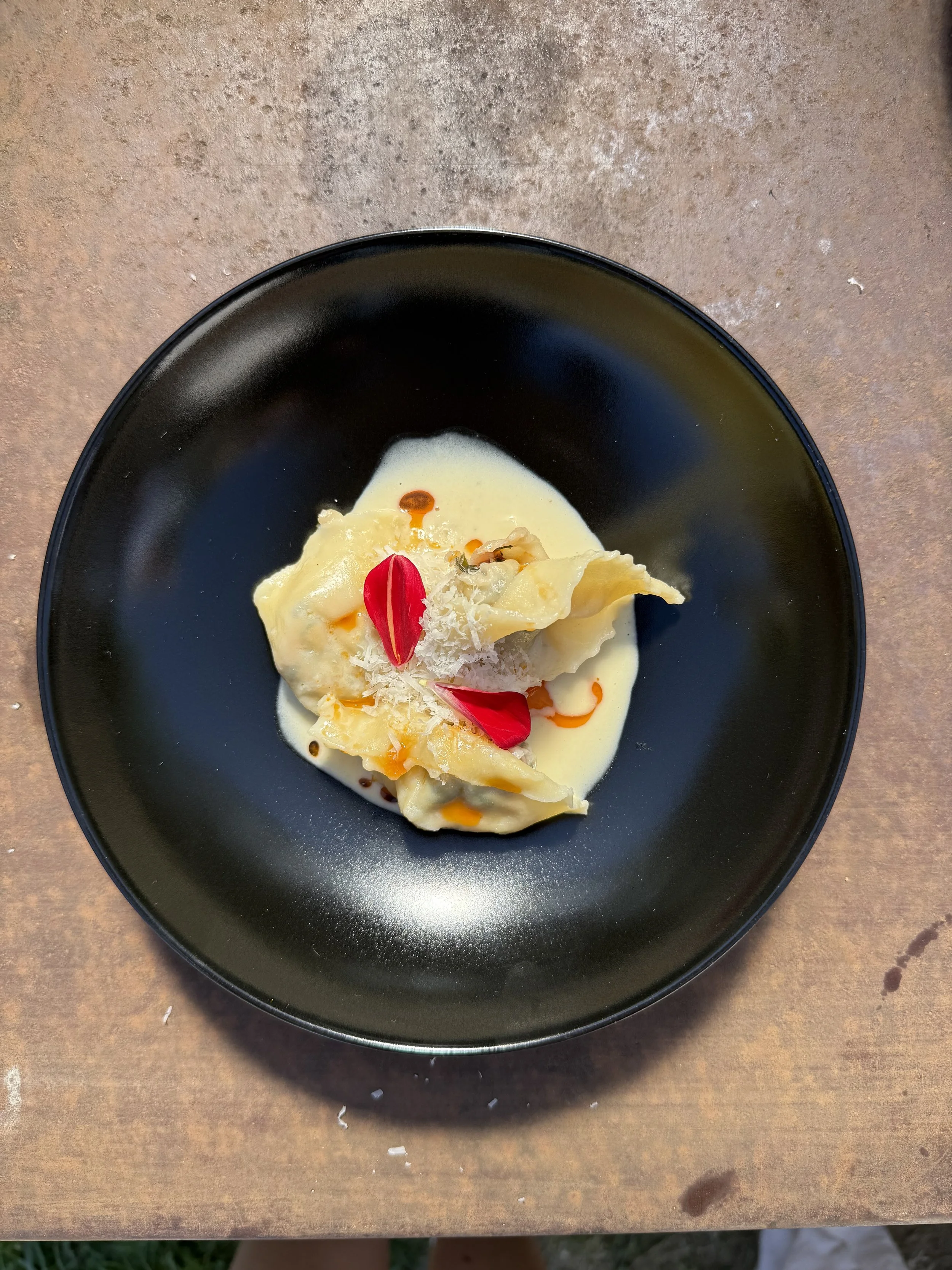 Ravioli mit heller Sauce und roten Blüten auf schwarzem Teller