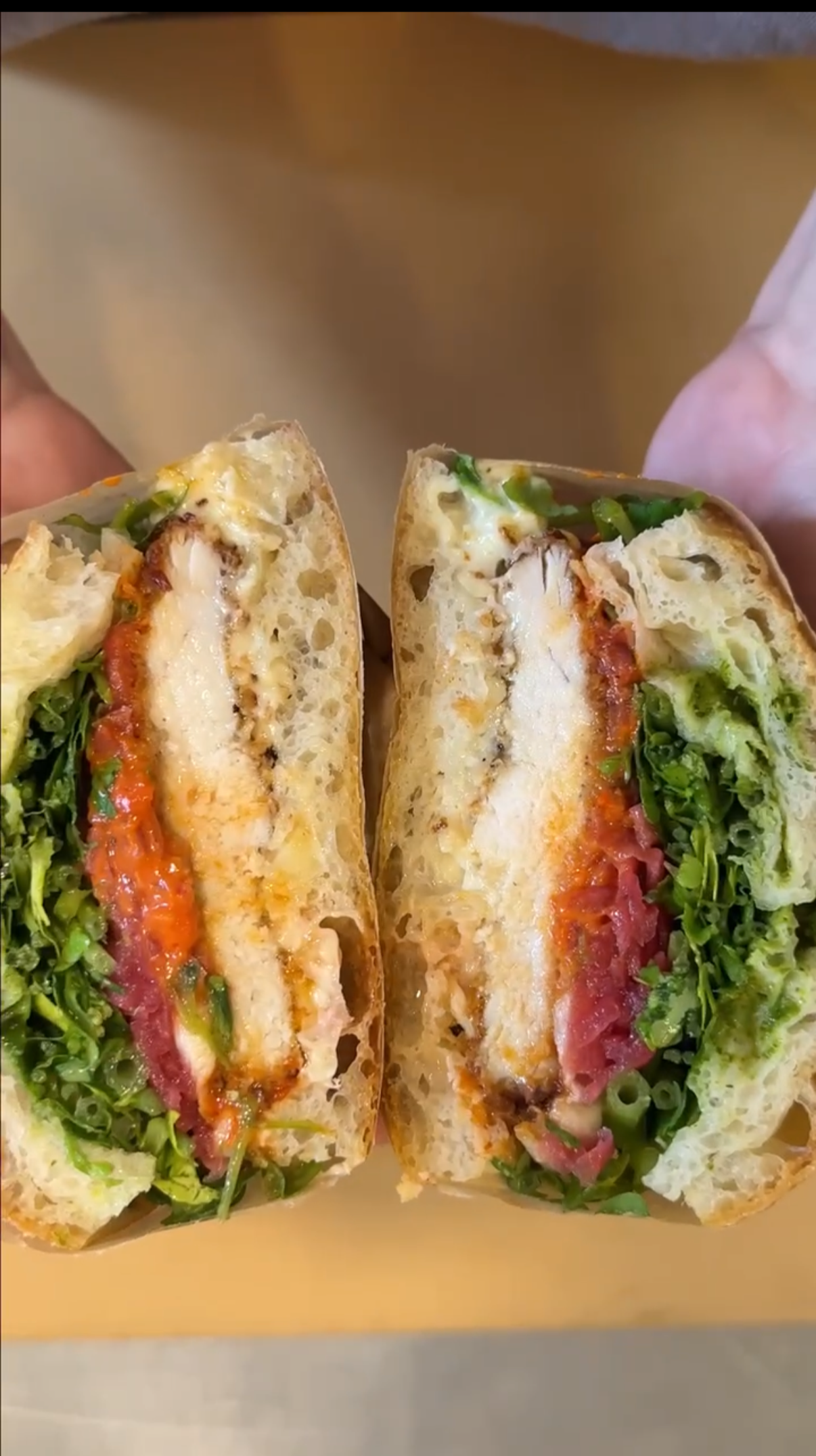 Ein halbiertes Focaccia Sandwich mit Hähnchen, Salat, Tomaten und Käse.