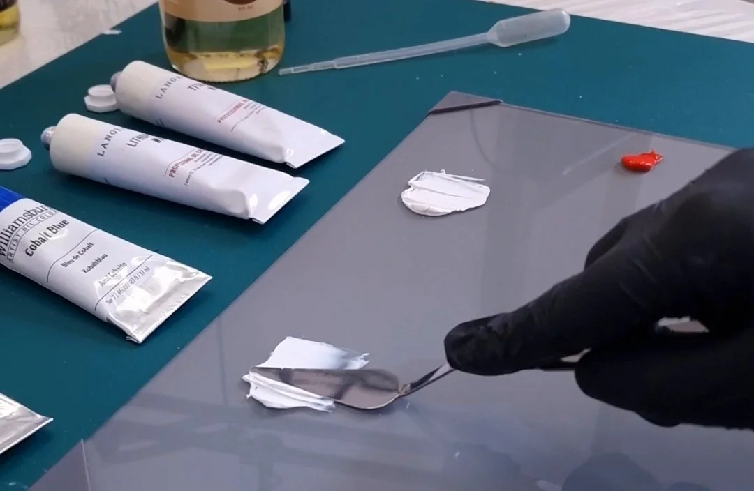Artist mixing professional oil paints with a palette knife during a technical material test in the studio.