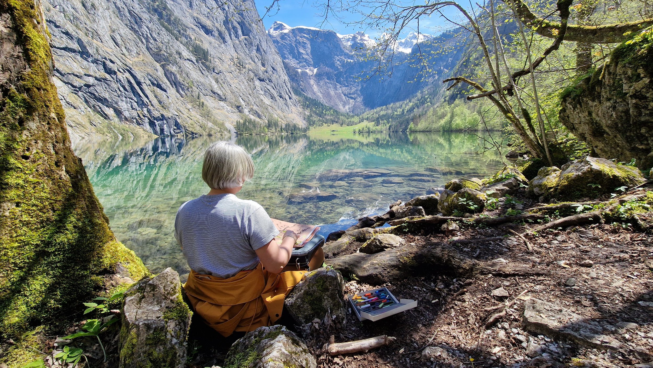 An artist sketching beside a mountain lake, observing the changing light and colours that become lasting visual memories.