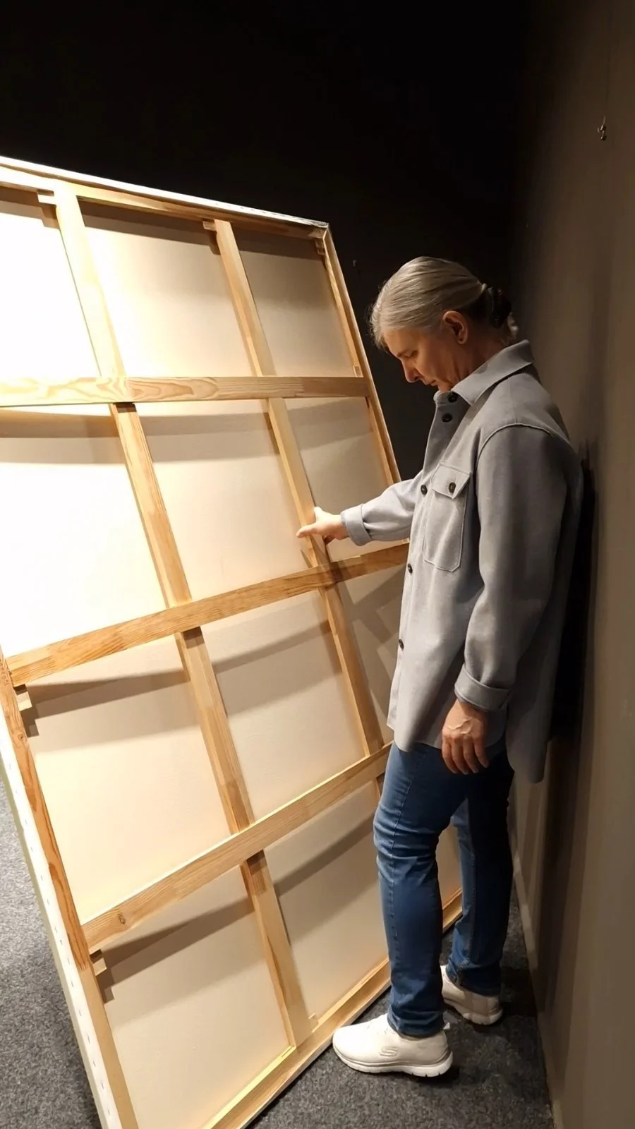 Contemporary oil painter standing beside the reverse of a large canvas in the studio, reflecting on artistic process and the relationship between artist and artwork.