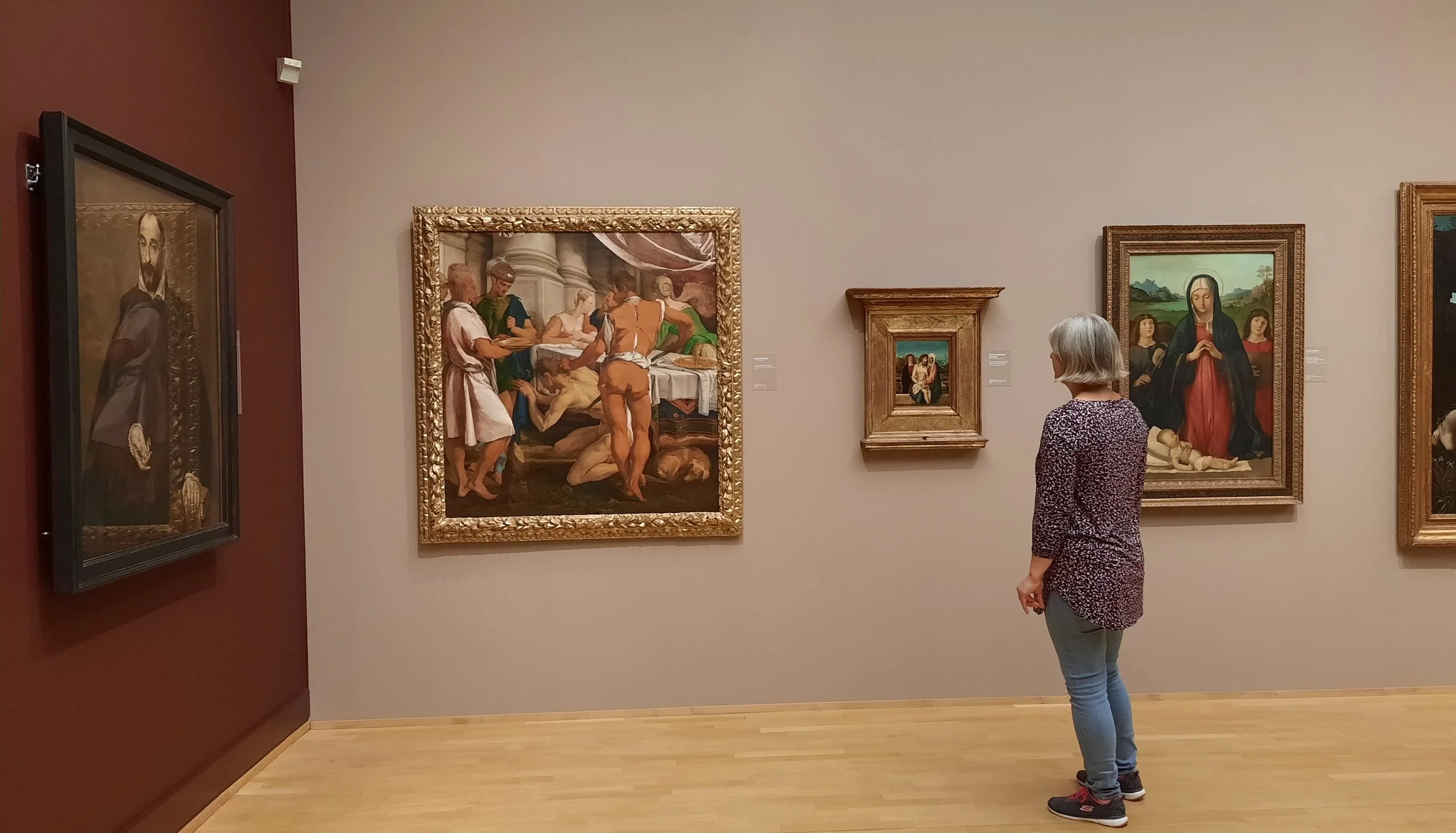 A museum visitor contemplating paintings at an art museum in Copenhagen, inviting reflection on how an artist's name and reputation shape the way we experience works of art.