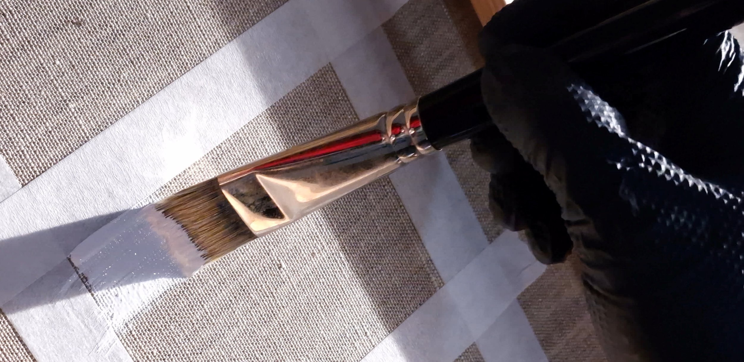 Brush applying white gesso to a linen canvas before an oil painting begins, illustrating the invisible foundation behind archival painting.