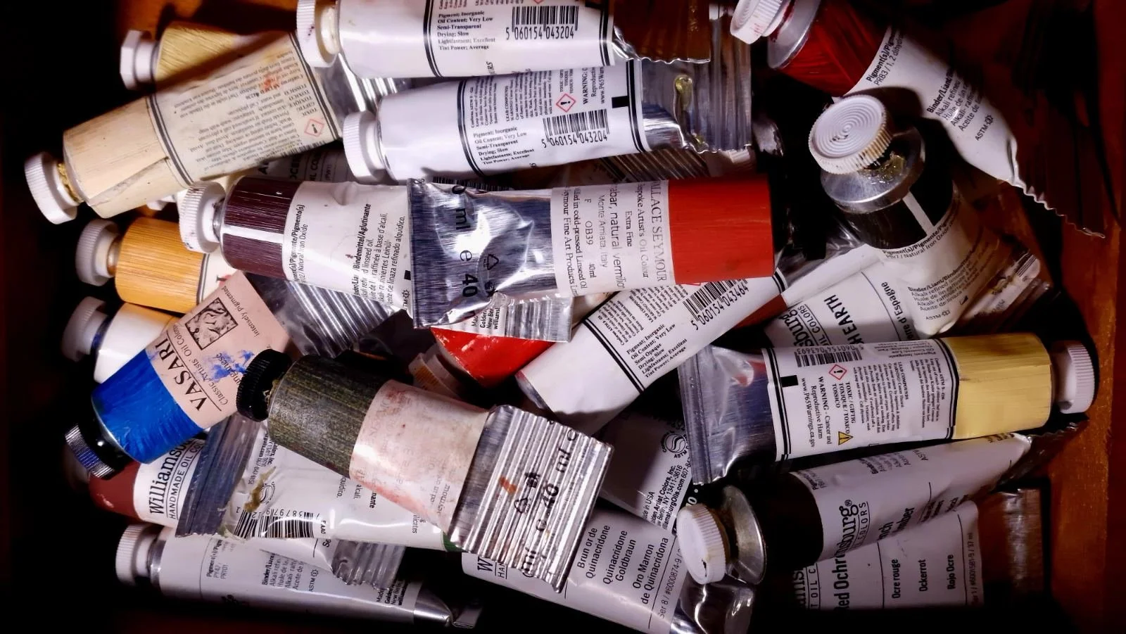 Used artists’ oil paint tubes gathered in a studio drawer, including natural vermilion and other traditional pigments, reflecting the material culture and technological heritage of painting.