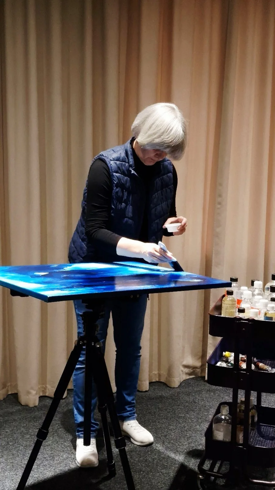An artist carefully applies a final protective varnish to a blue abstract oil painting in her studio, enhancing the depth of colour and surface finish.