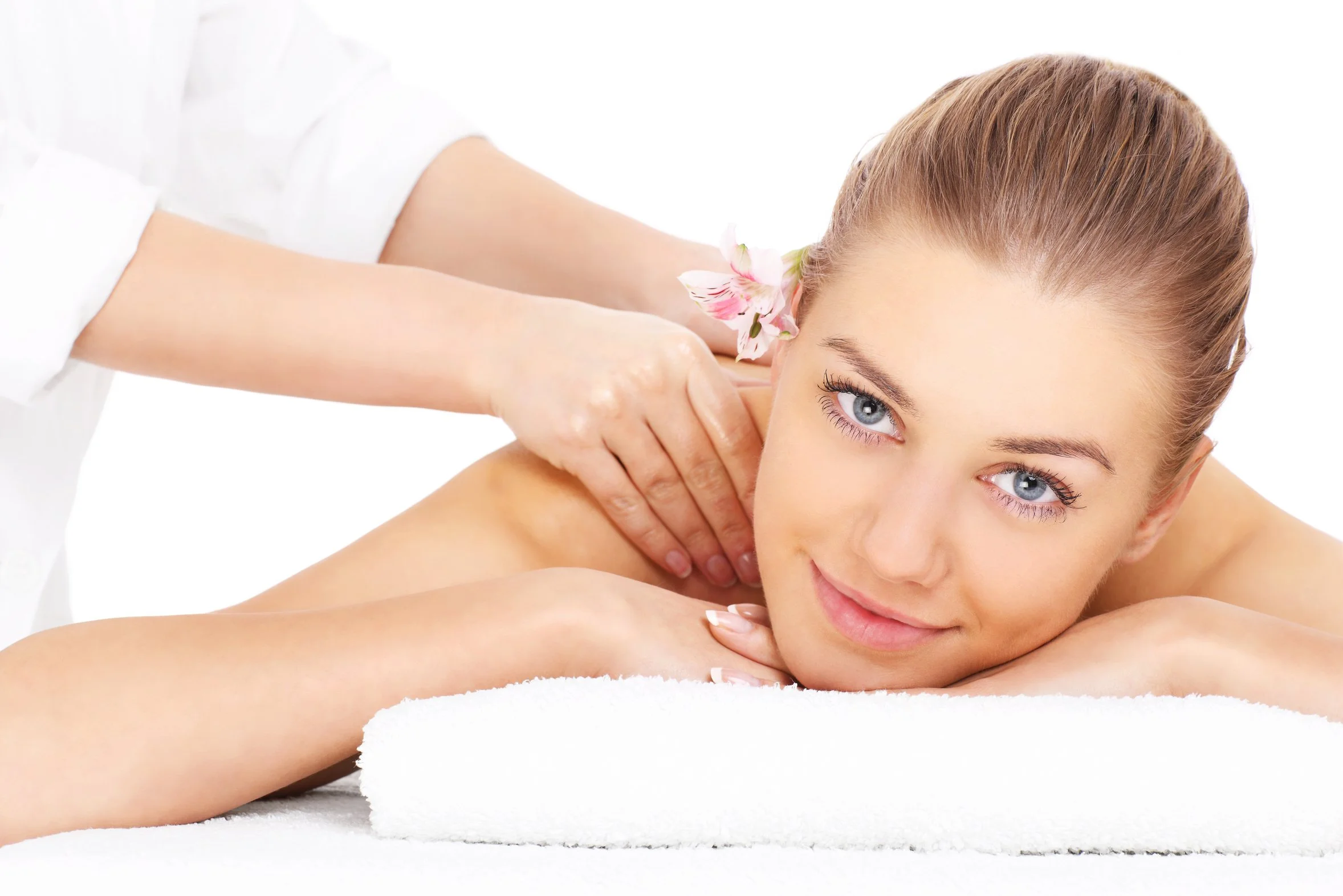 Une femme recevant un massage en position allongée sur une table de massage, avec un décor blanc, accompagnée d'une touche de fleurs roses dans les cheveux.