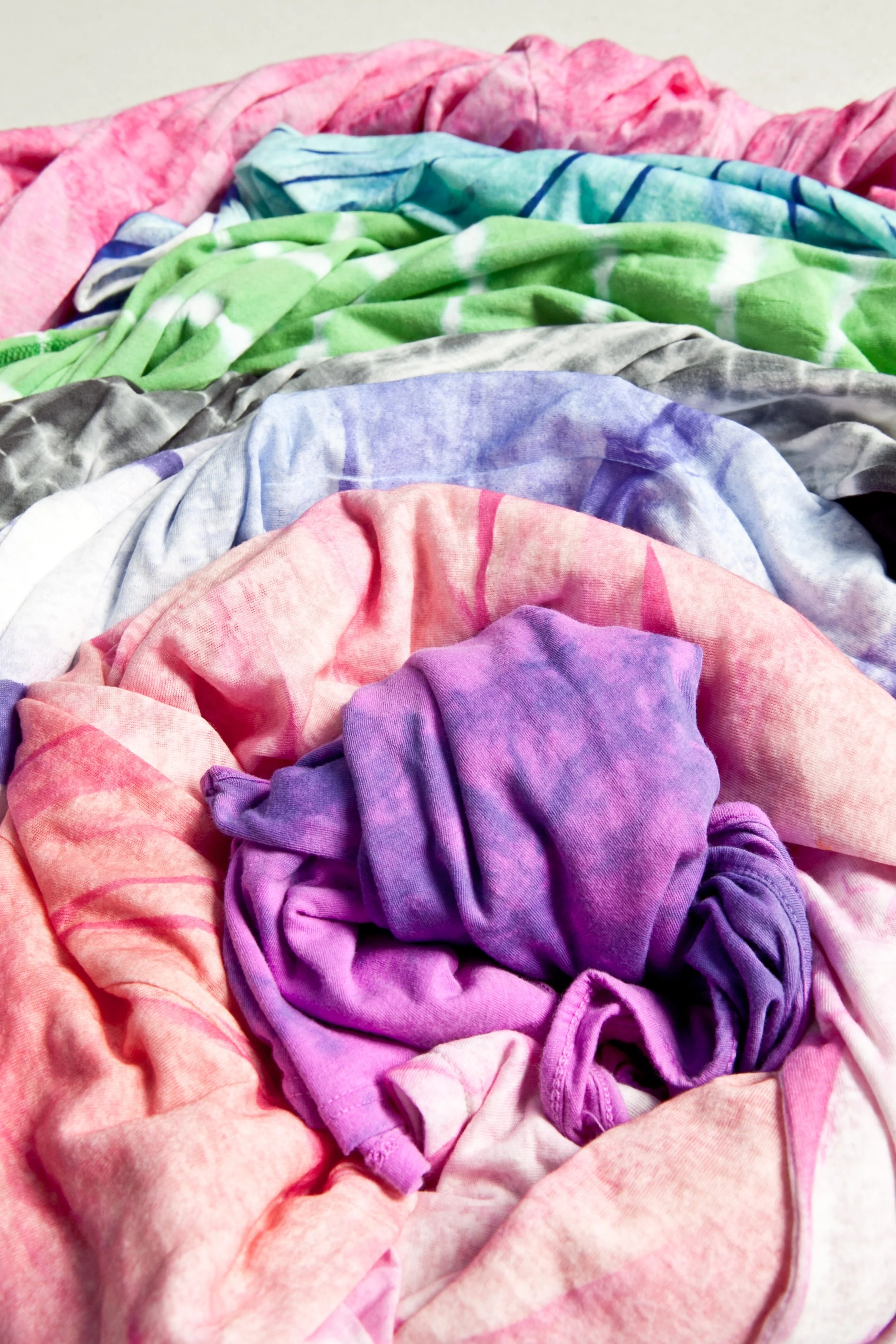 Colorful, crumpled tie-dye cloths in shades of pink, purple, blue, green, and gray.