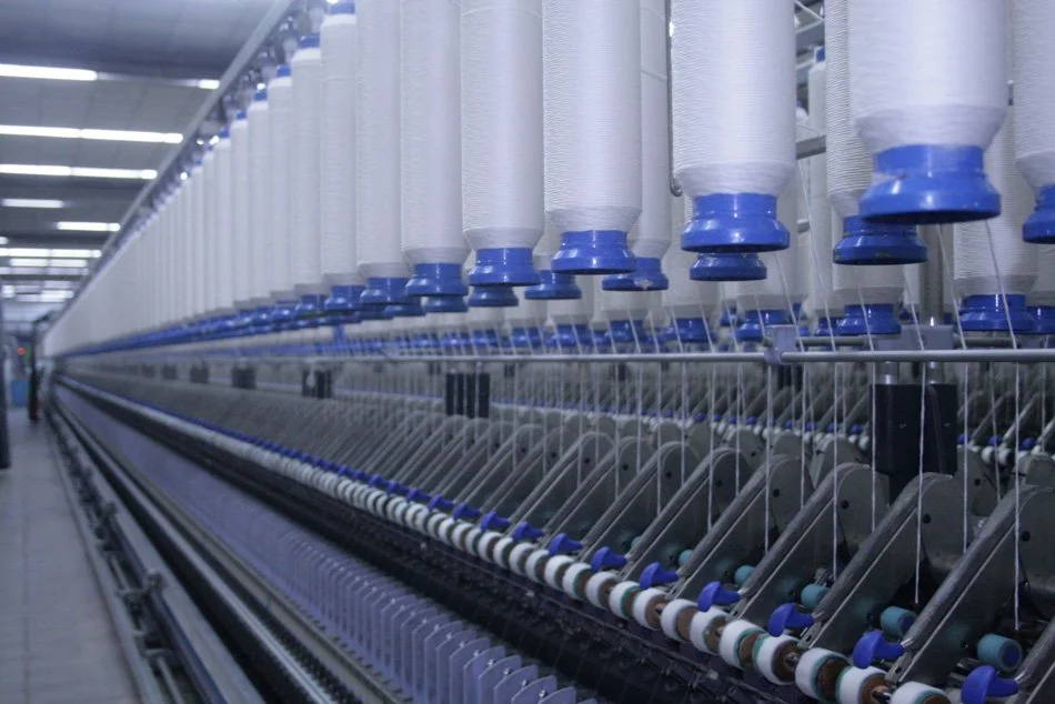 Close-up view of spinning machine with multiple spools of white thread in a textile manufacturing facility.