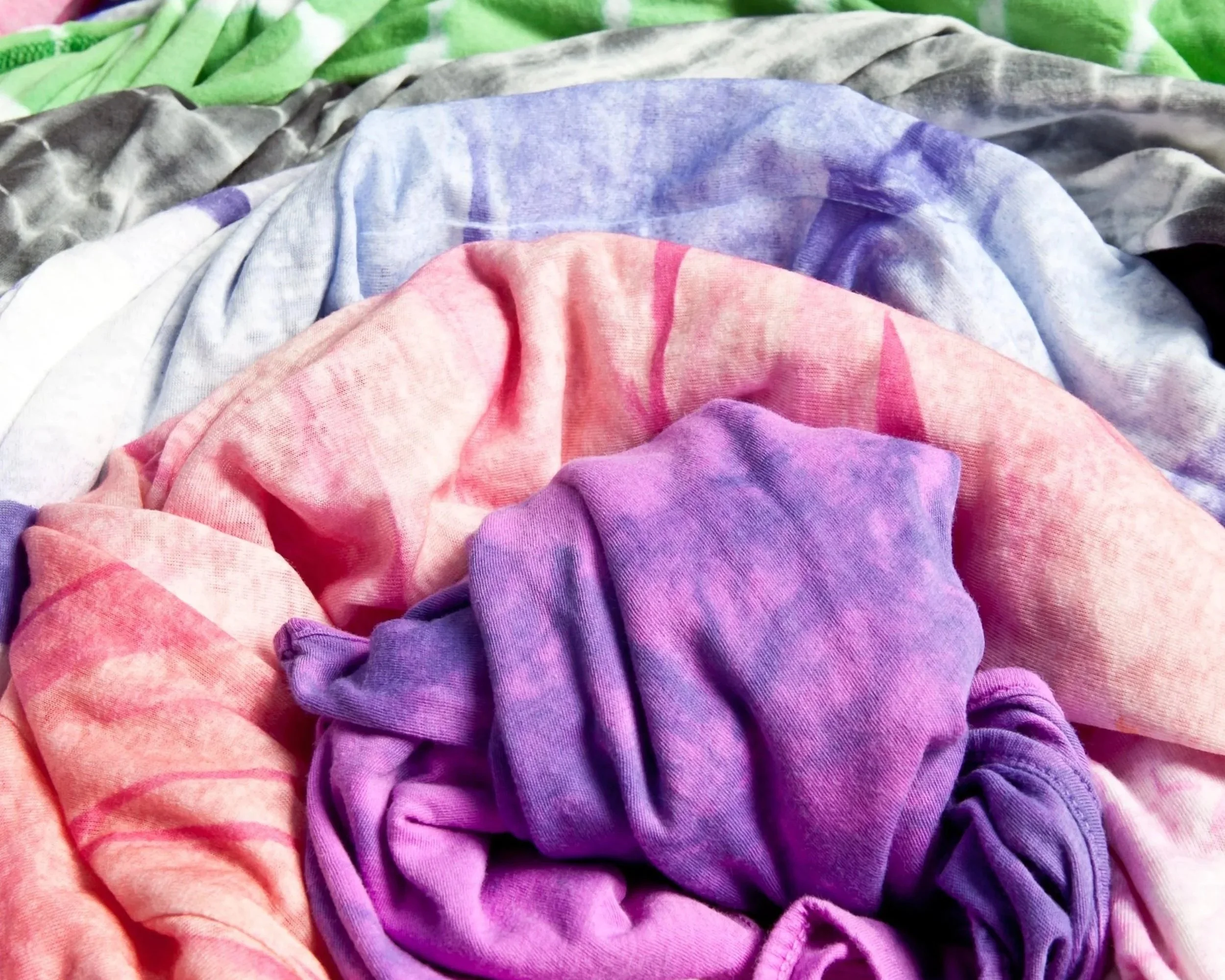 Close-up of colorful fabric, including pink, purple, blue, gray, and green pieces, arranged casually.