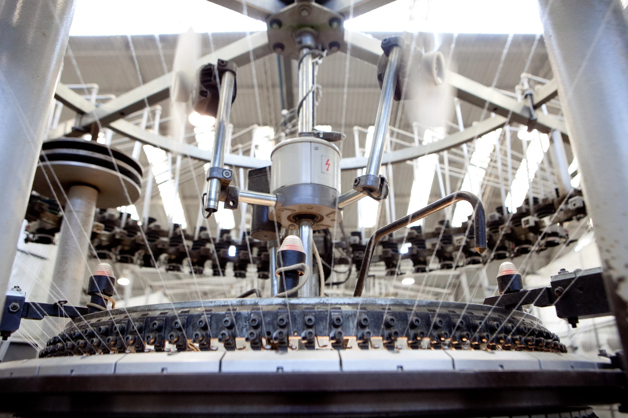 Close-up of a textile machine used for manufacturing fabric or yarn, with metal components, spools, and threads.