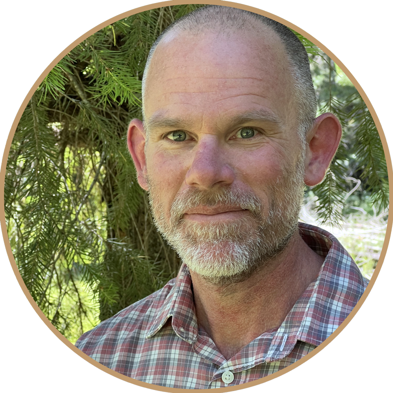 Headshot of Mike Short, founder of Raven Property Watch, wearing a plaid shirt, standing outdoors near green trees.