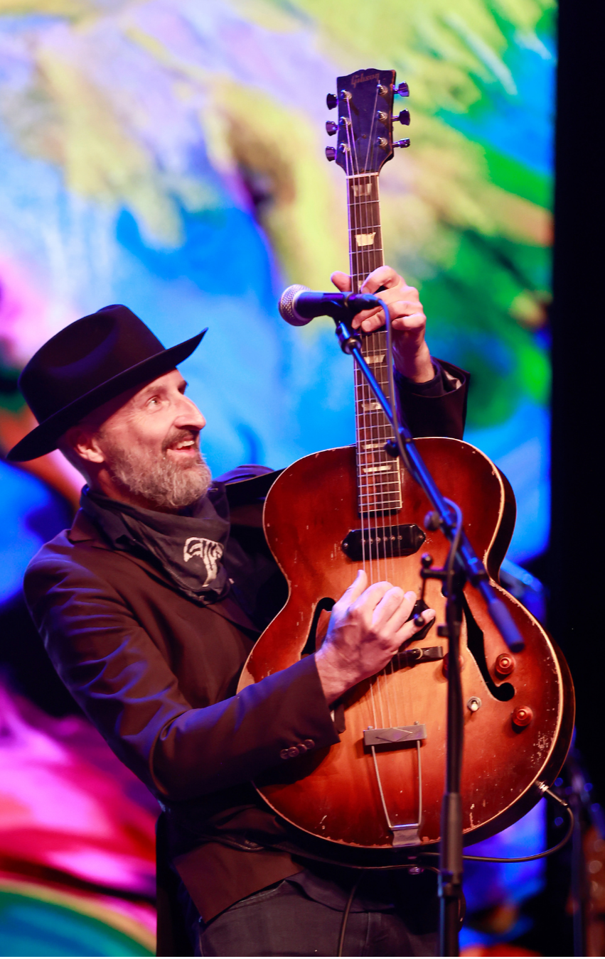 Man wearing black hat and black jacket playing a vintage brown hollow-body electric guitar on stage in West Tennessee at The Dixie PAC