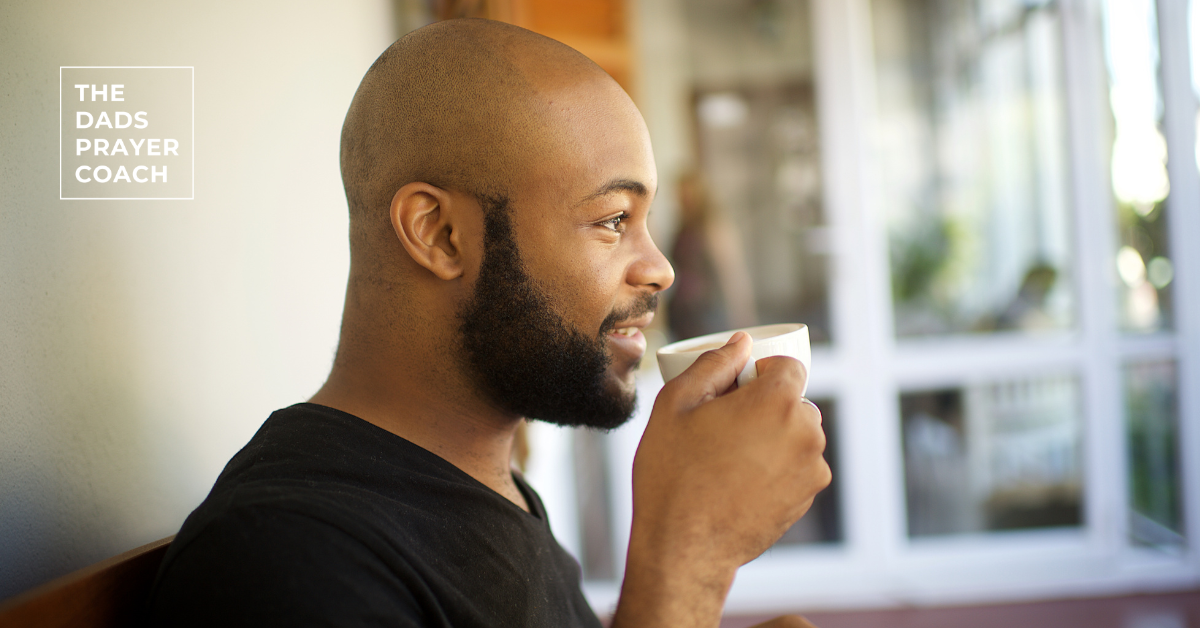 Black man with a beard sitting on a porch sipping a cup of coffee