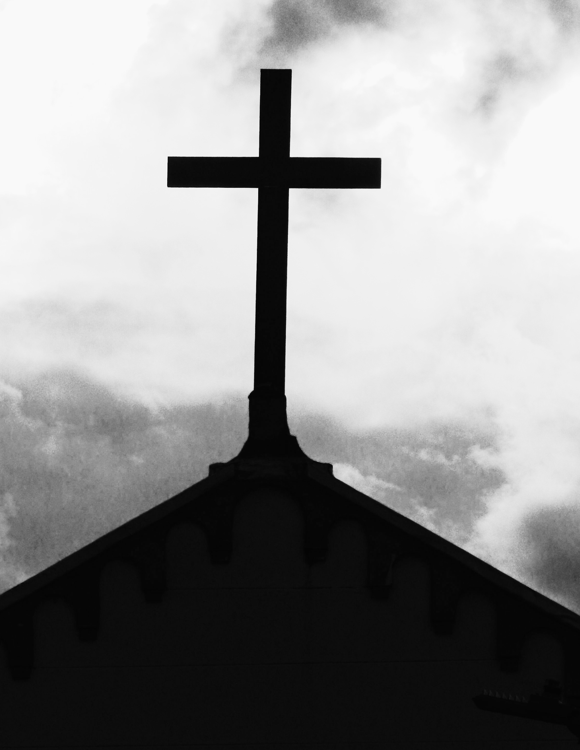 Picture of a church steeple with a cross at the peek rising above the roof line, dark clouds in the background.
