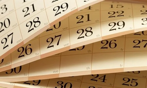 Close-up of multiple curled paper calendars showing dates in black ink