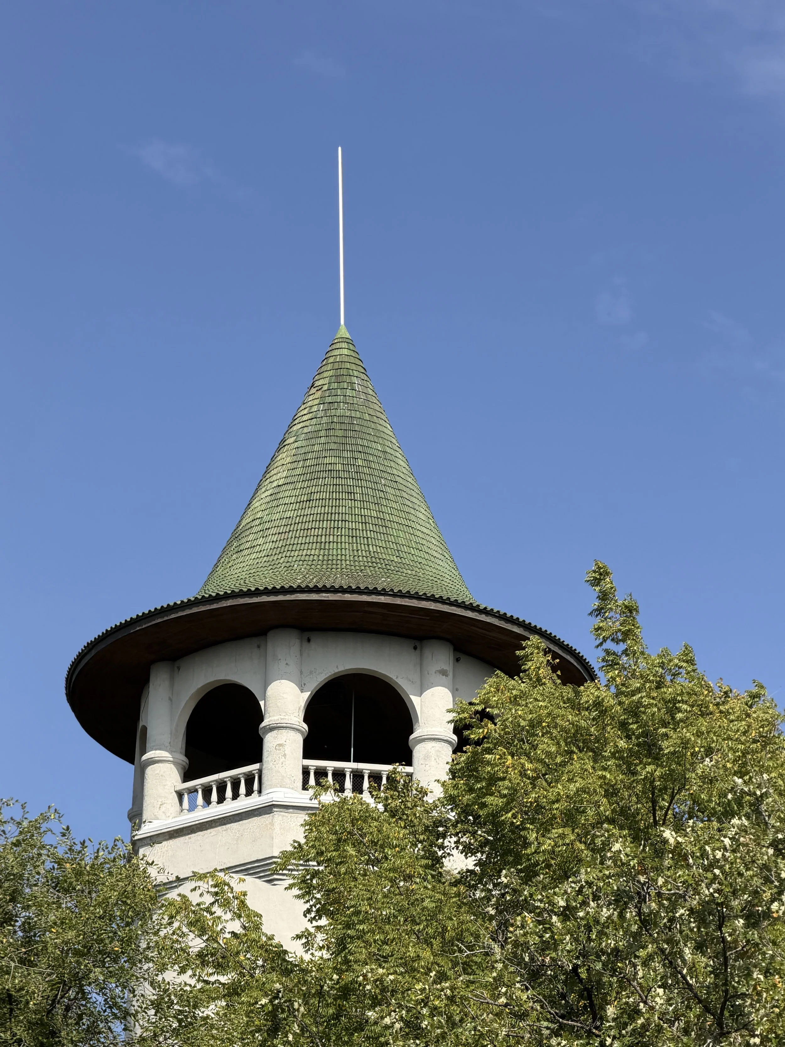 The Prospect Park Water Tower in Minneapolis, with a green tiled roof rising into a clear blue sky, surrounded by green trees.