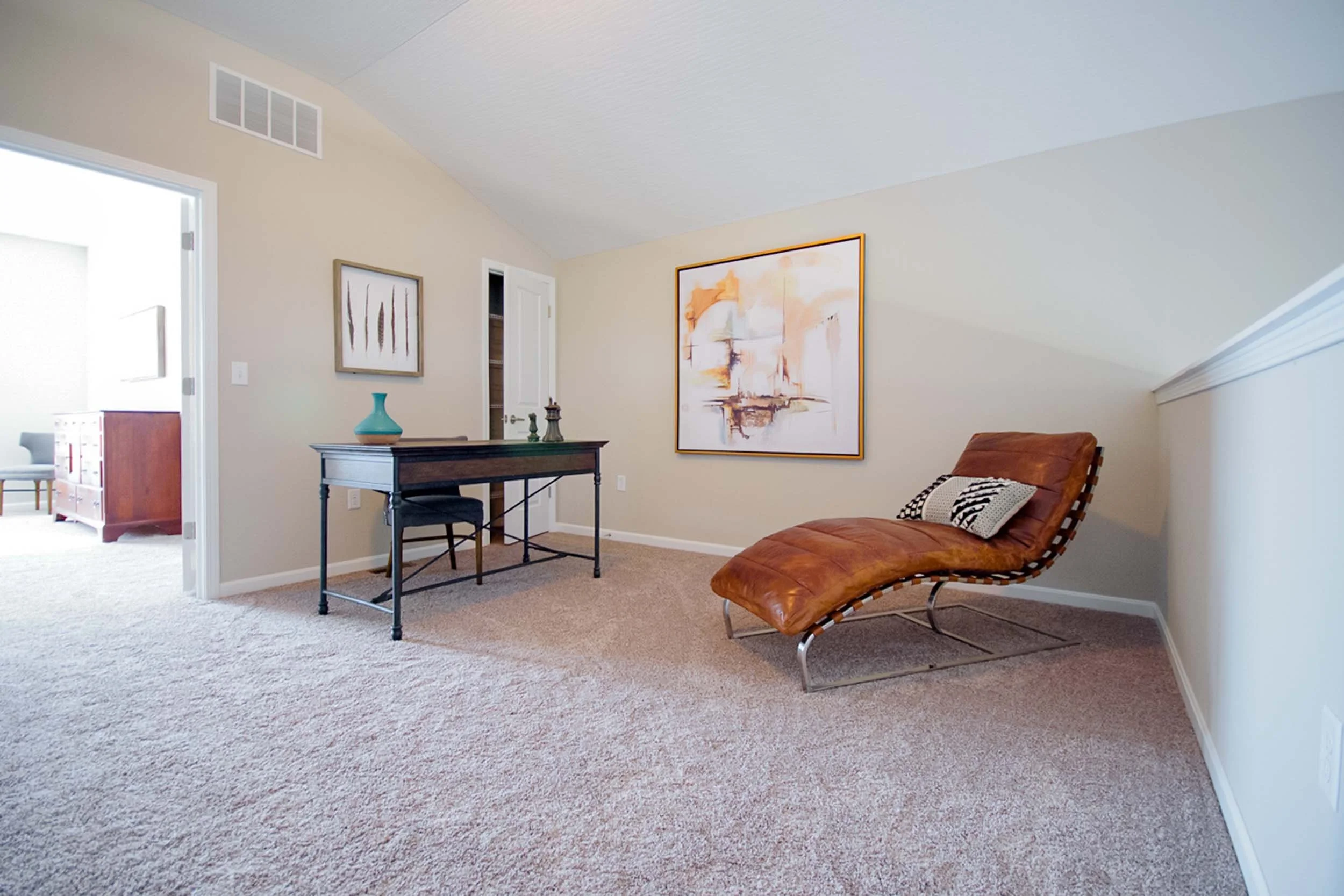 Living room with beige walls, artwork on the walls, and a leather lounge chair with a black-and-white pillow.