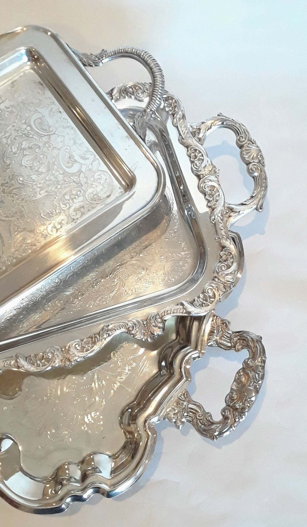 Close-up of ornate silver serving tray with intricate floral and scroll patterns, decorative handles, and a raised edge, featuring a rectangular container with engraved details.