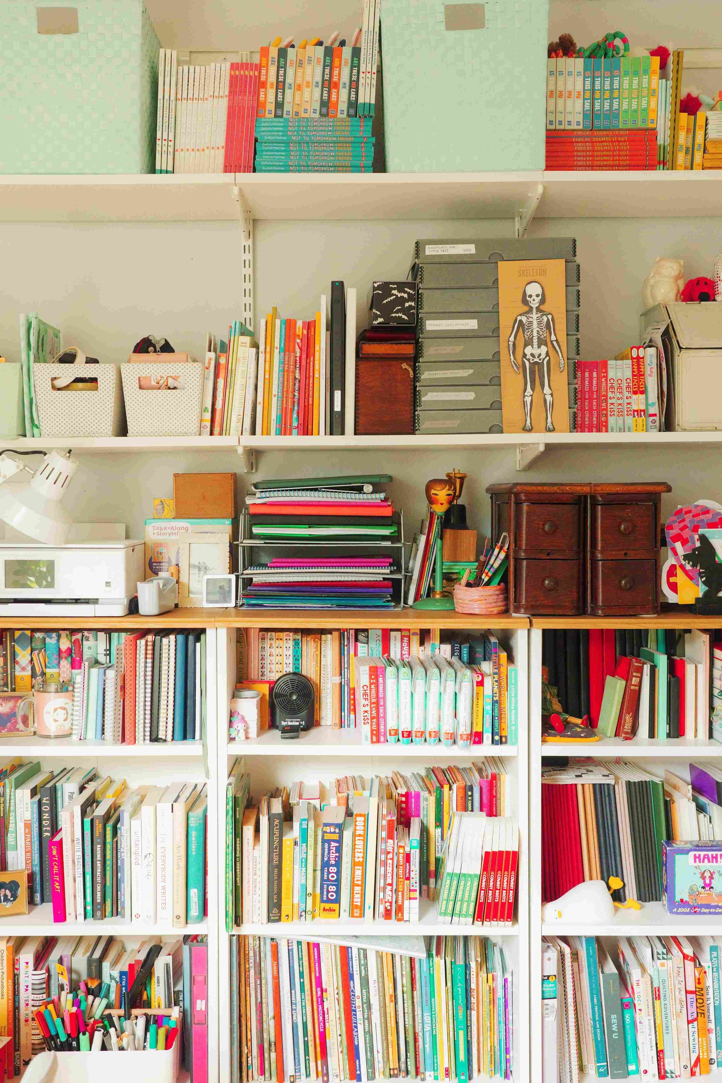 Shelf in Denise Holmes’ illustration studio with children’s books, artwork, and creative supplies used for her projects.