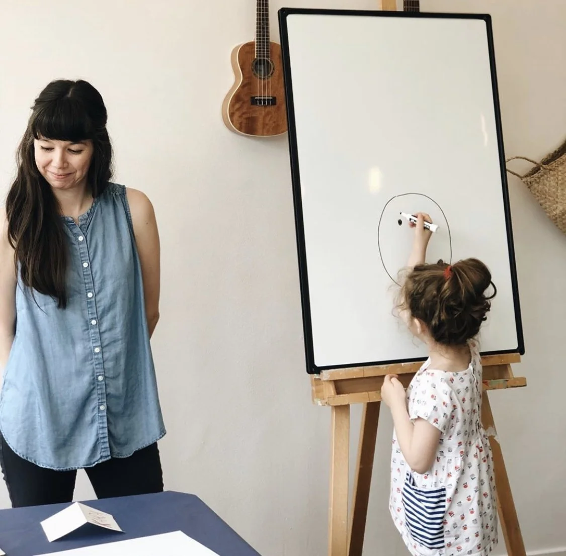 Denise Holmes leading a children's drawing workshop with a young participant creating artwork at a table.