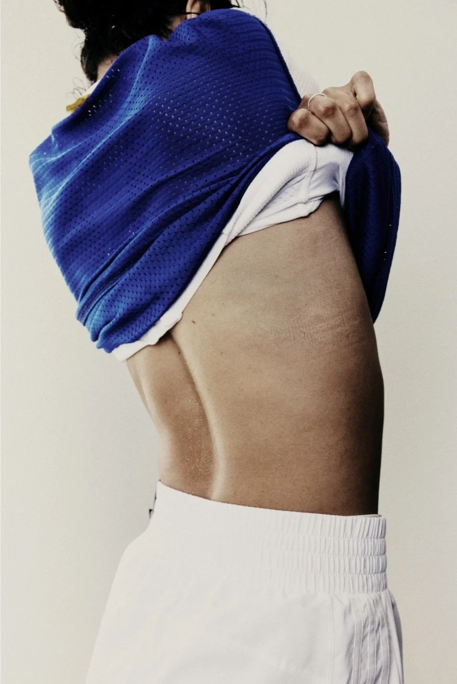 Person lifting a blue sports jersey, revealing their bare midriff and white athletic shorts.