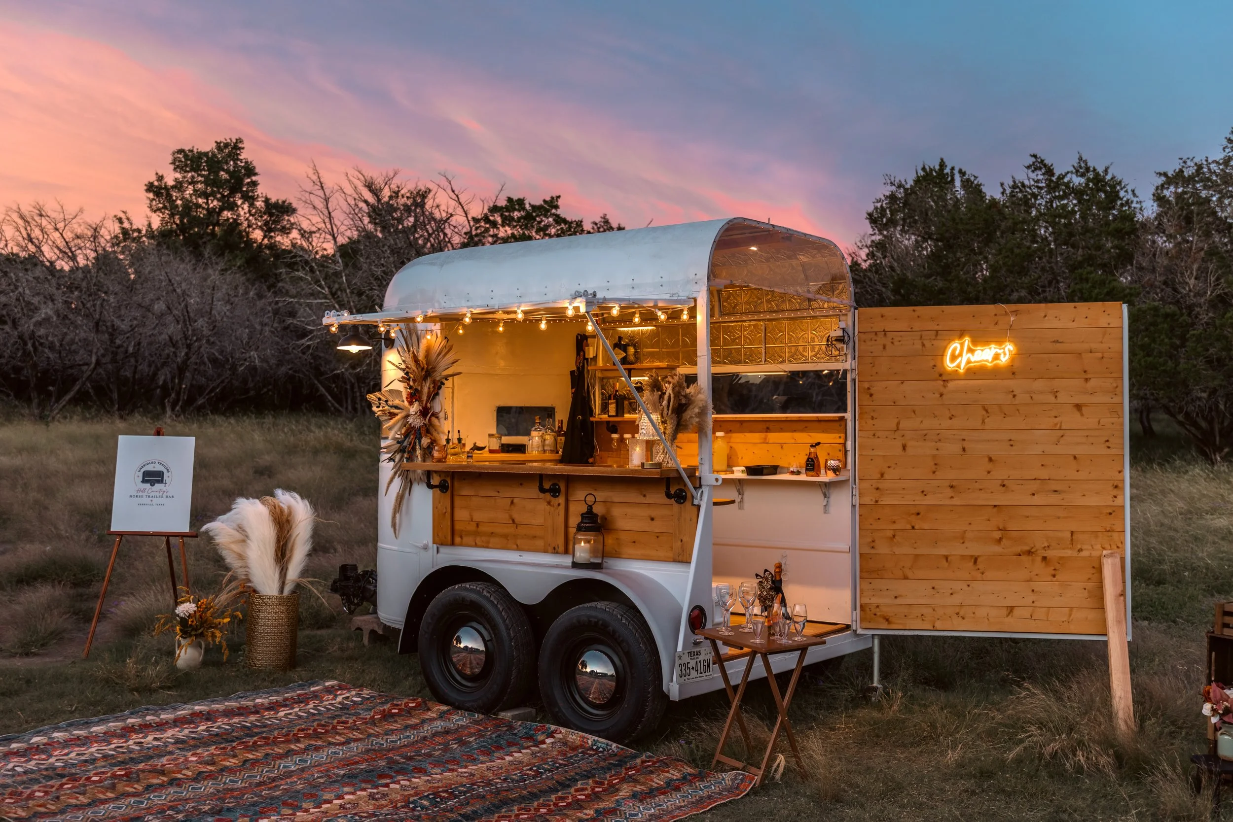 A mobile bar setup inside a small trailer decorated with string lights, with a