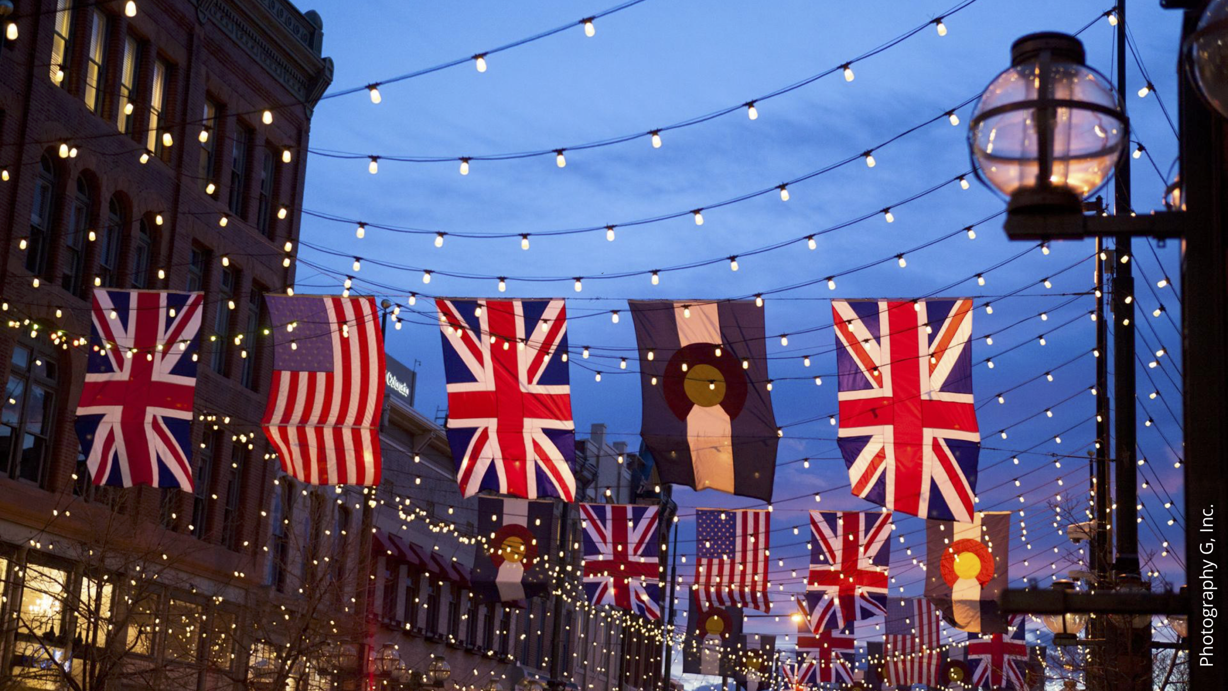Street decorated with British flags and string lights hanging from buildings and street lamps during dusk.