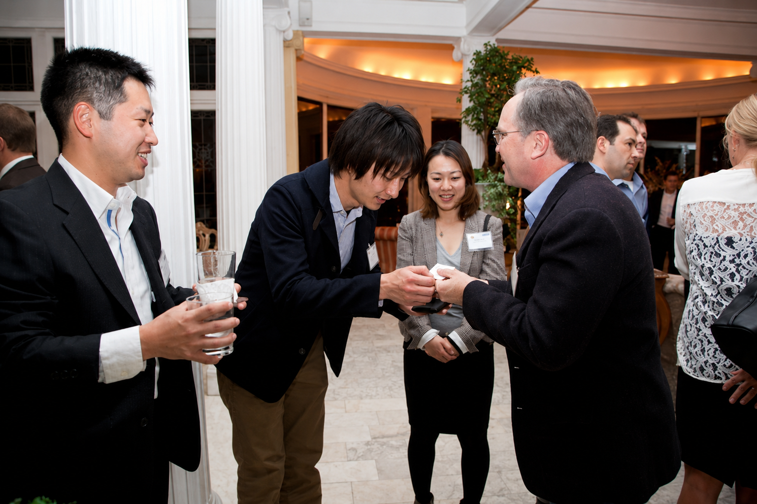 Business people socializing at a formal event, talking, and holding drinks in a well-lit, elegant venue.