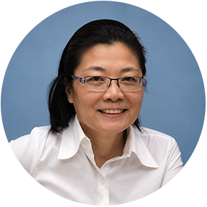 A woman with black hair and glasses, wearing a white shirt, smiling against a blue background.