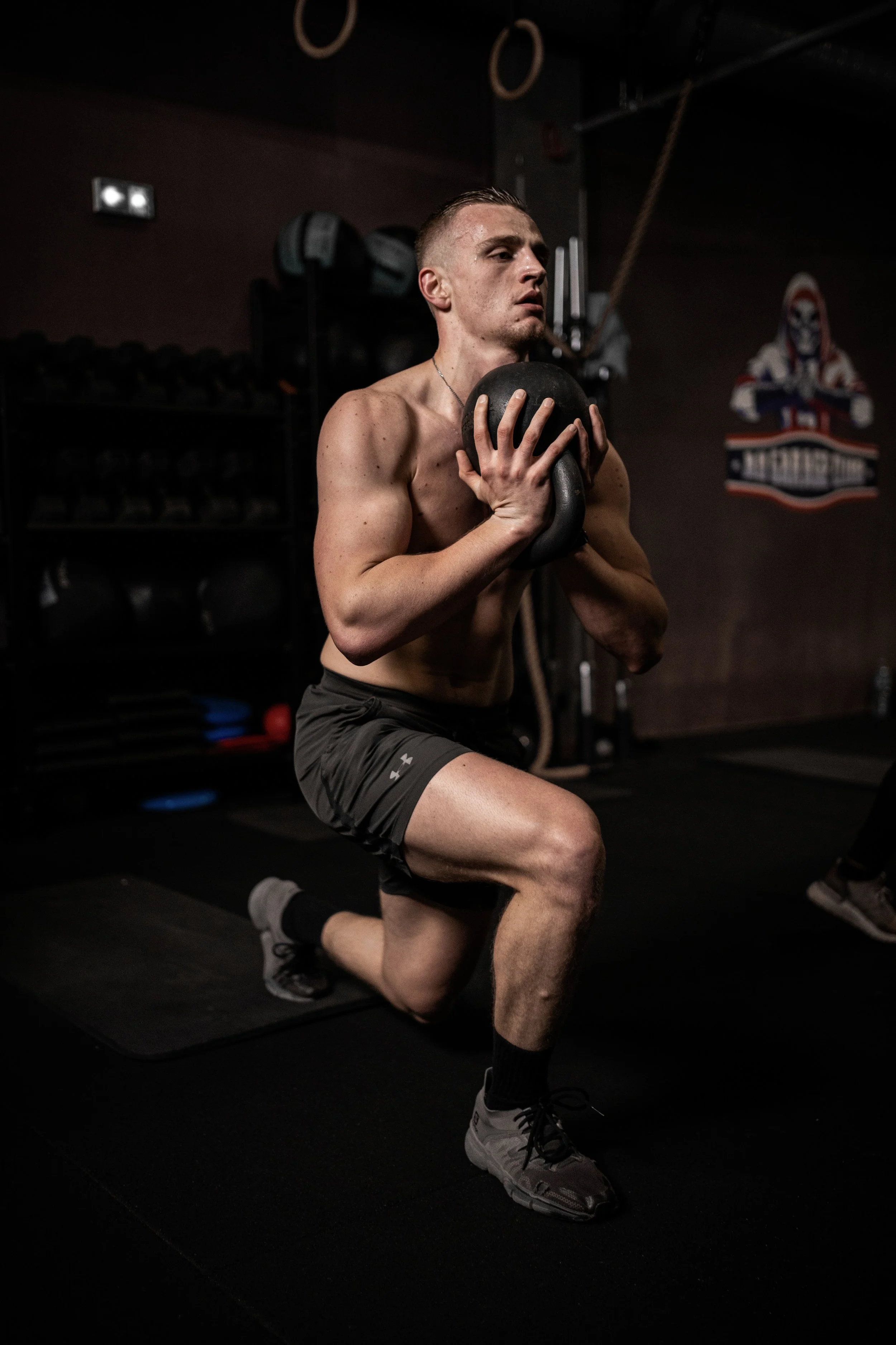 Homme musclé faisant une flexion au genou en tenant une kettlebell contre sa poitrine dans une salle de sport