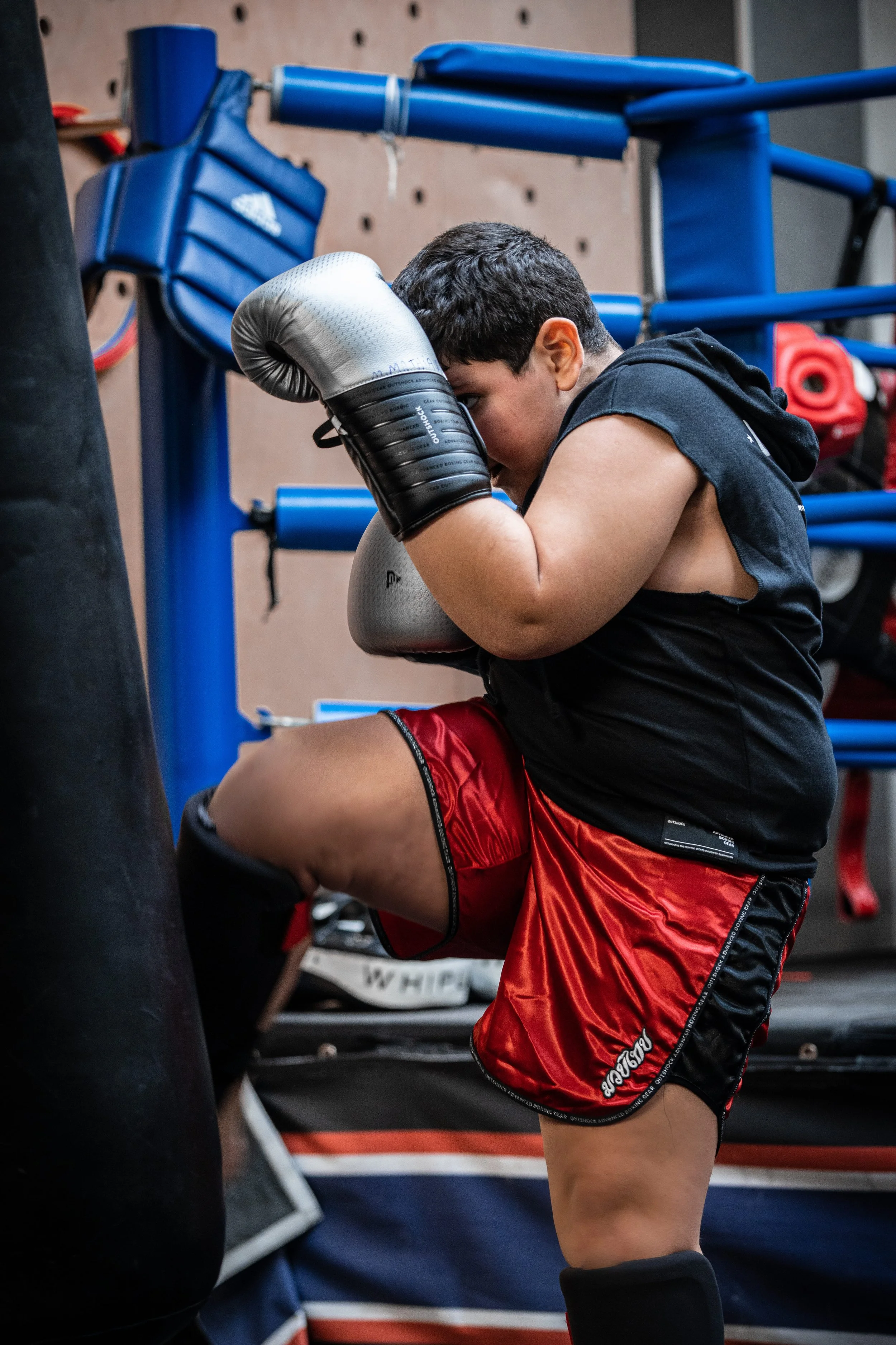 Un jeune boxeur en entraînement dans un gymnase, portant des vêtements de sport rouges et noirs, avec des gants de boxe argentés, se préparant pour un entraînement ou un combat.
