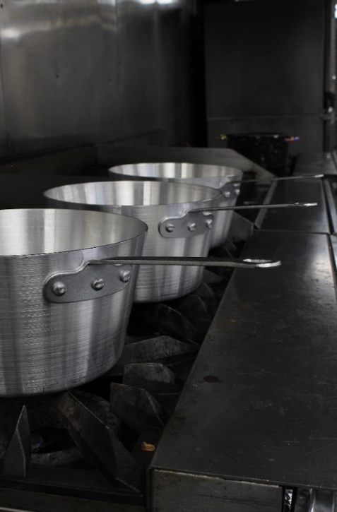 Three large aluminum pots on a stovetop in a commercial kitchen.
