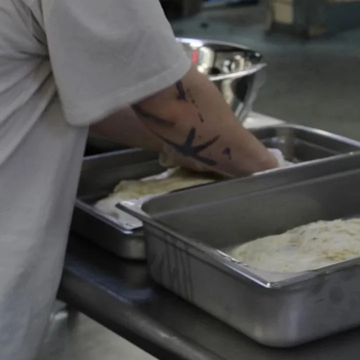 Person with tattoos on arm preparing food in stainless steel trays.