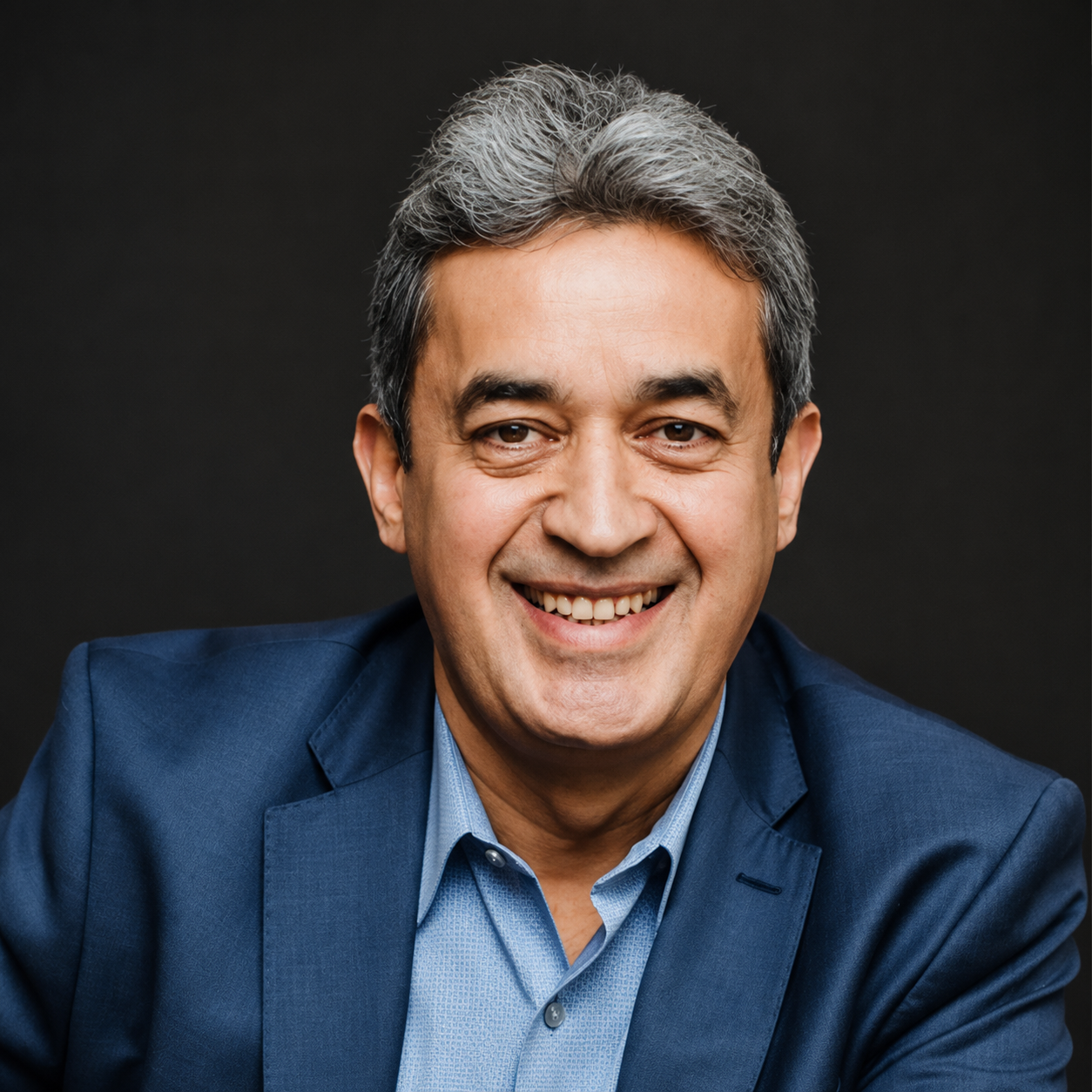 A smiling man with gray hair in a blue suit and light blue shirt against a dark background.