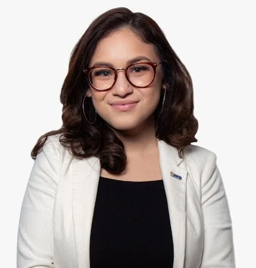 Woman with brown hair, glasses, wearing a white blazer and black top, smiling against a plain white background.