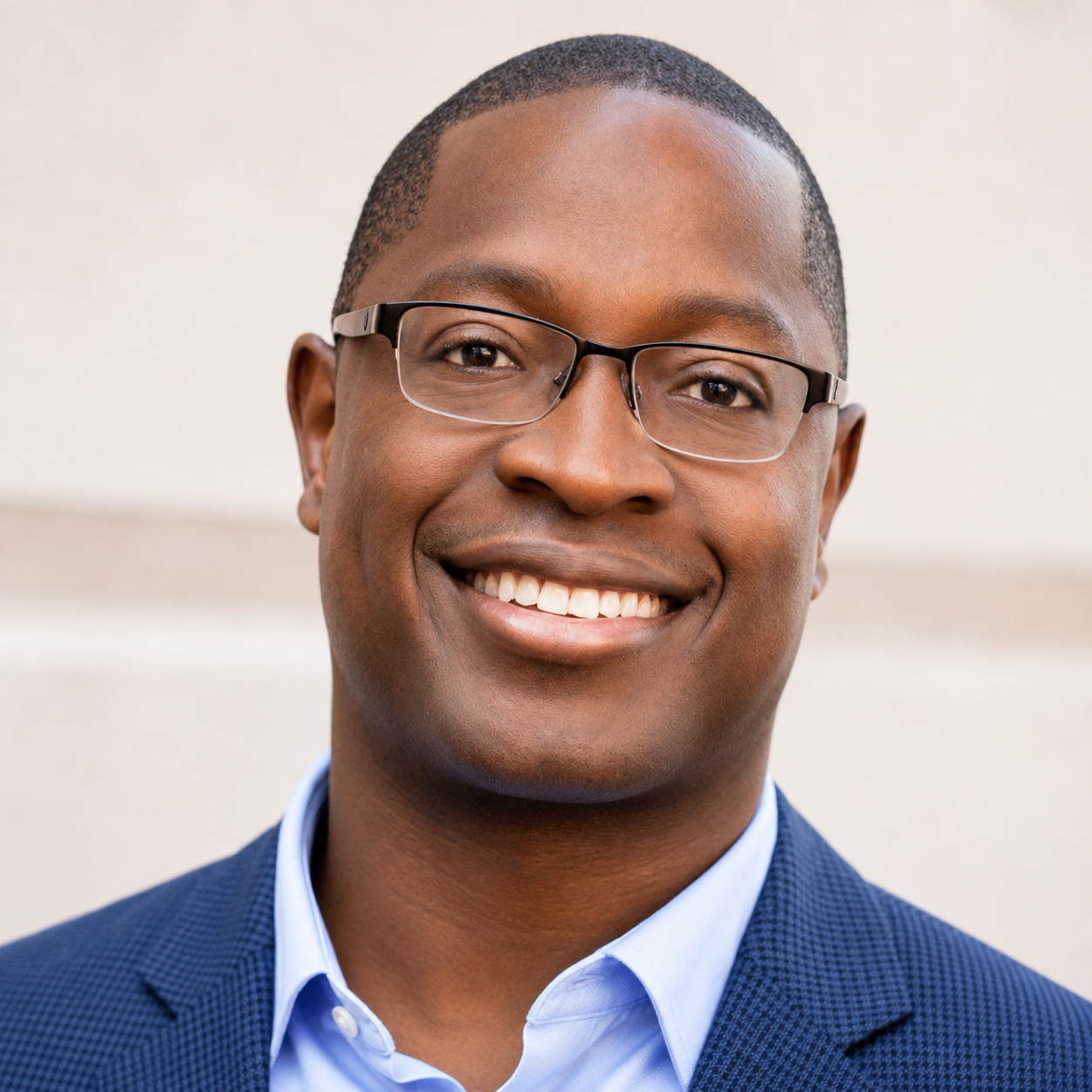 A smiling man wearing glasses, a blue suit, and a light blue shirt.