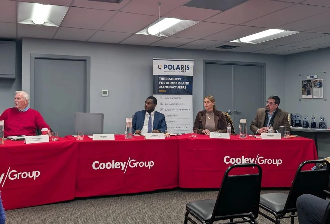 Four people seated at a long red table with Cooley/Group branding during a panel discussion or meeting.