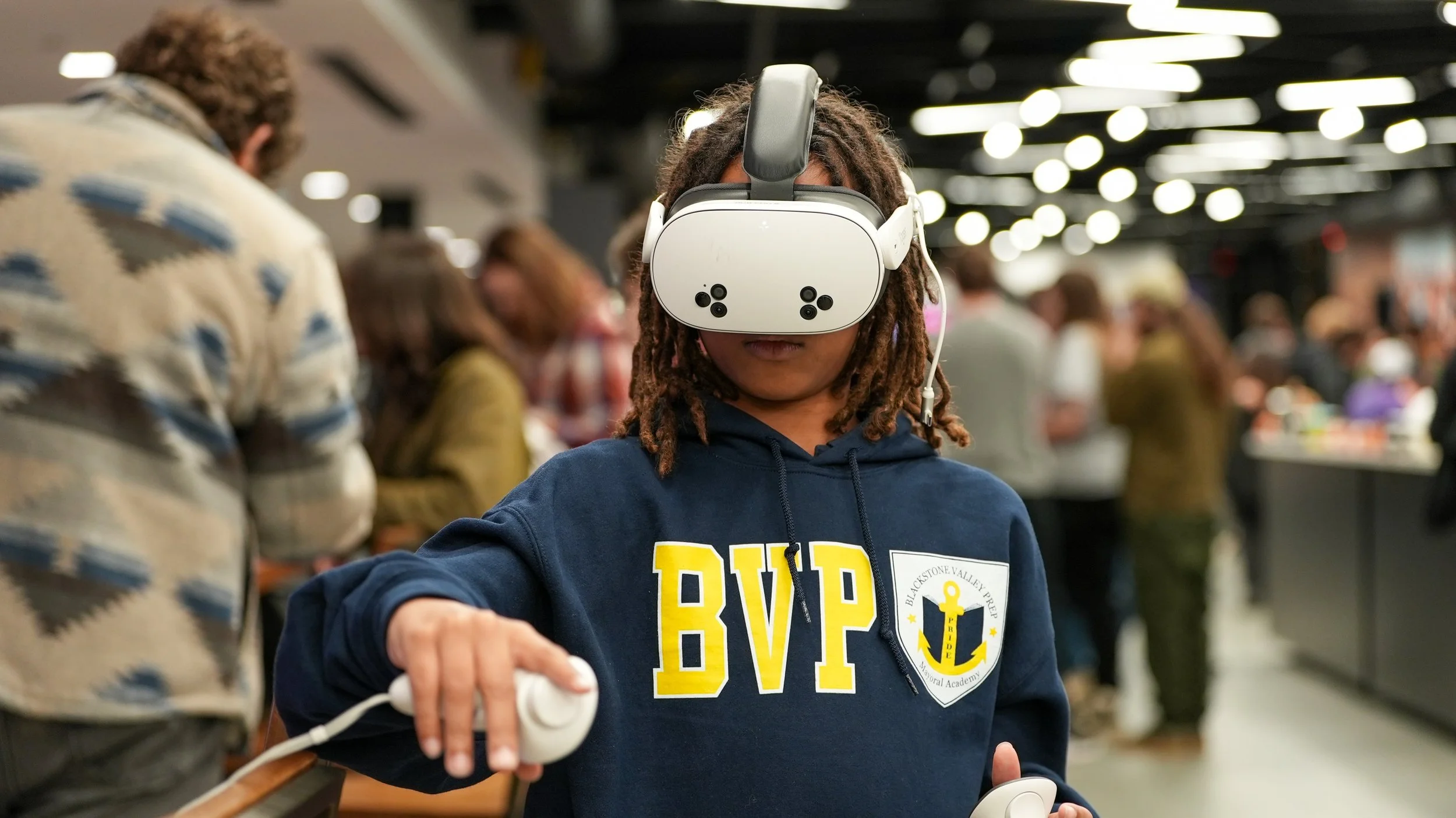 A person with dreadlocks wearing a virtual reality headset in a crowded indoor space.