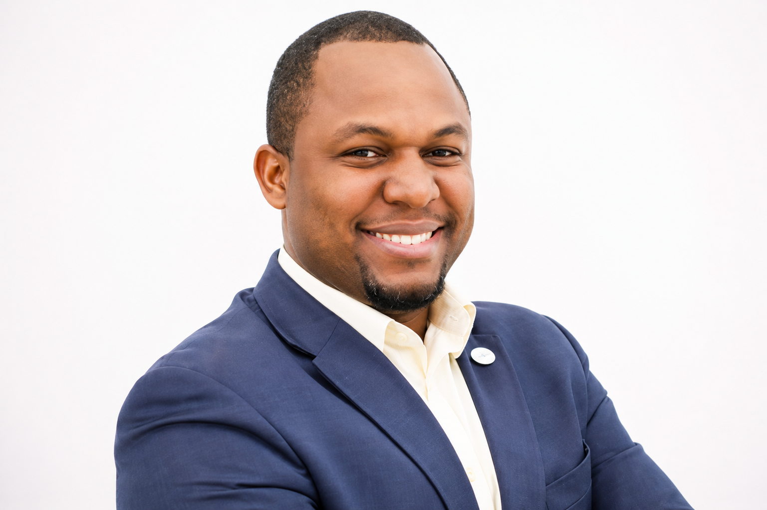 Professional man smiling in a navy suit and white shirt against a plain white background.