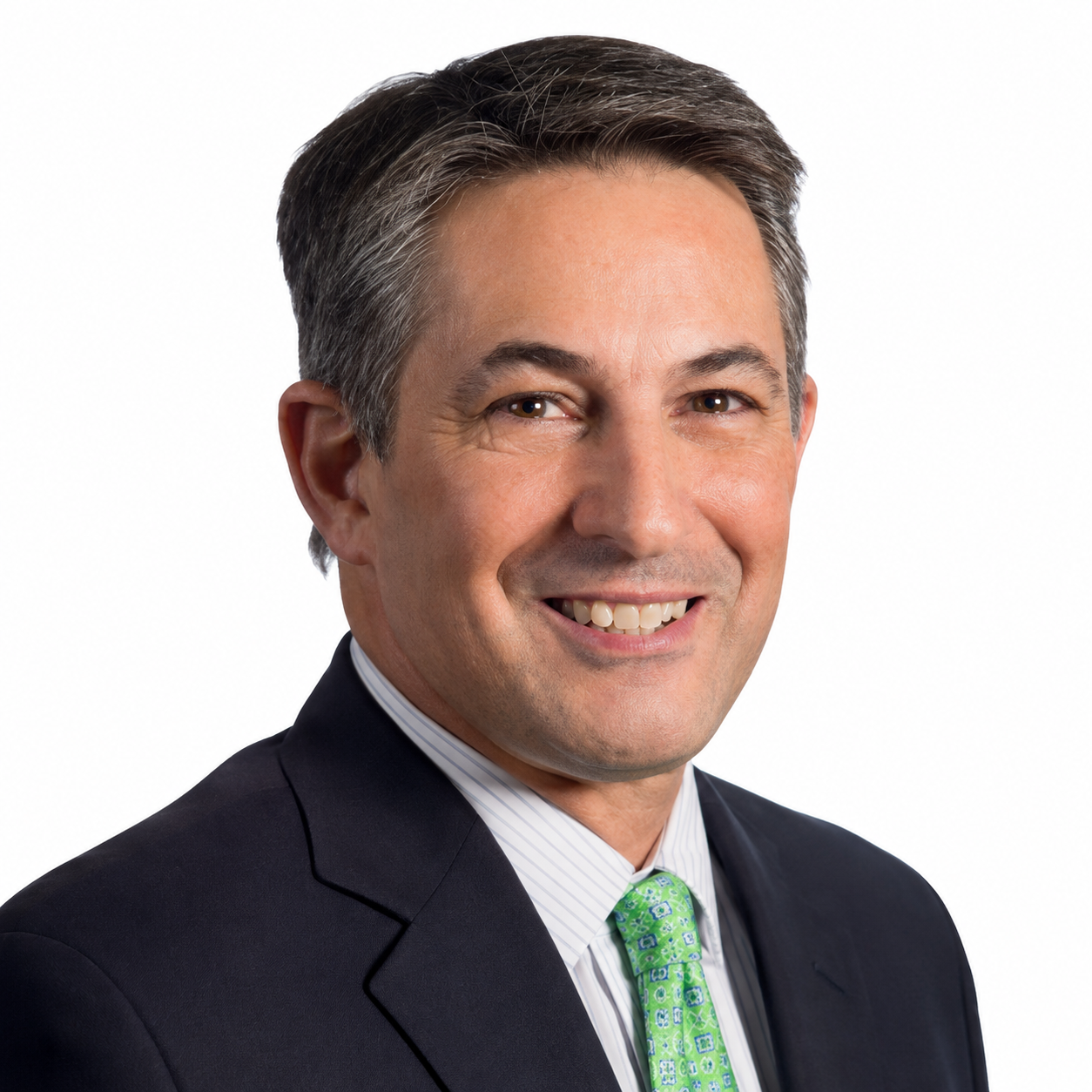 A smiling middle-aged man with dark and gray hair, wearing a dark suit, white shirt, and green patterned tie, against a plain white background.