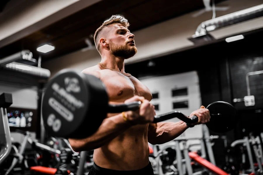 A muscular man is lifting a barbell with weights at a gym, focusing intently on his workout.
