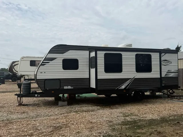A black and white travel trailer with three windows parked on a gravel lot.