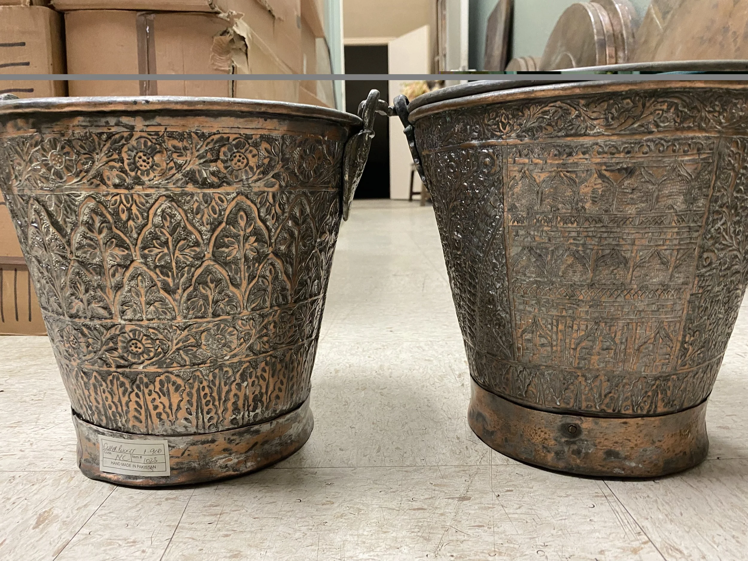 Two intricately carved traditional Desi brass buckets with floral and geometric patterns, placed on a tiled floor.