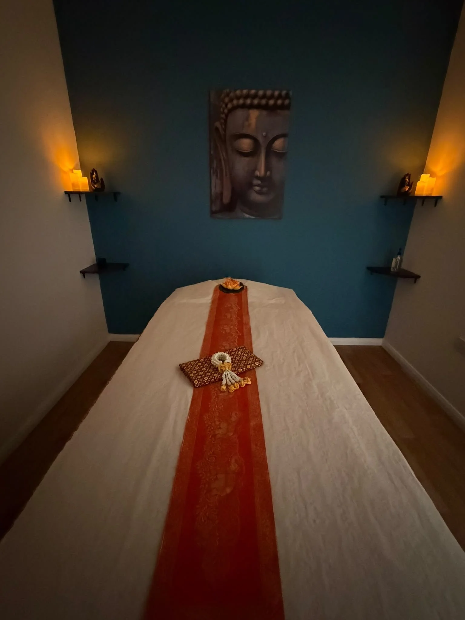 A serene meditation room with a Buddha painting on a blue wall and soft candle lighting on black floating shelves.