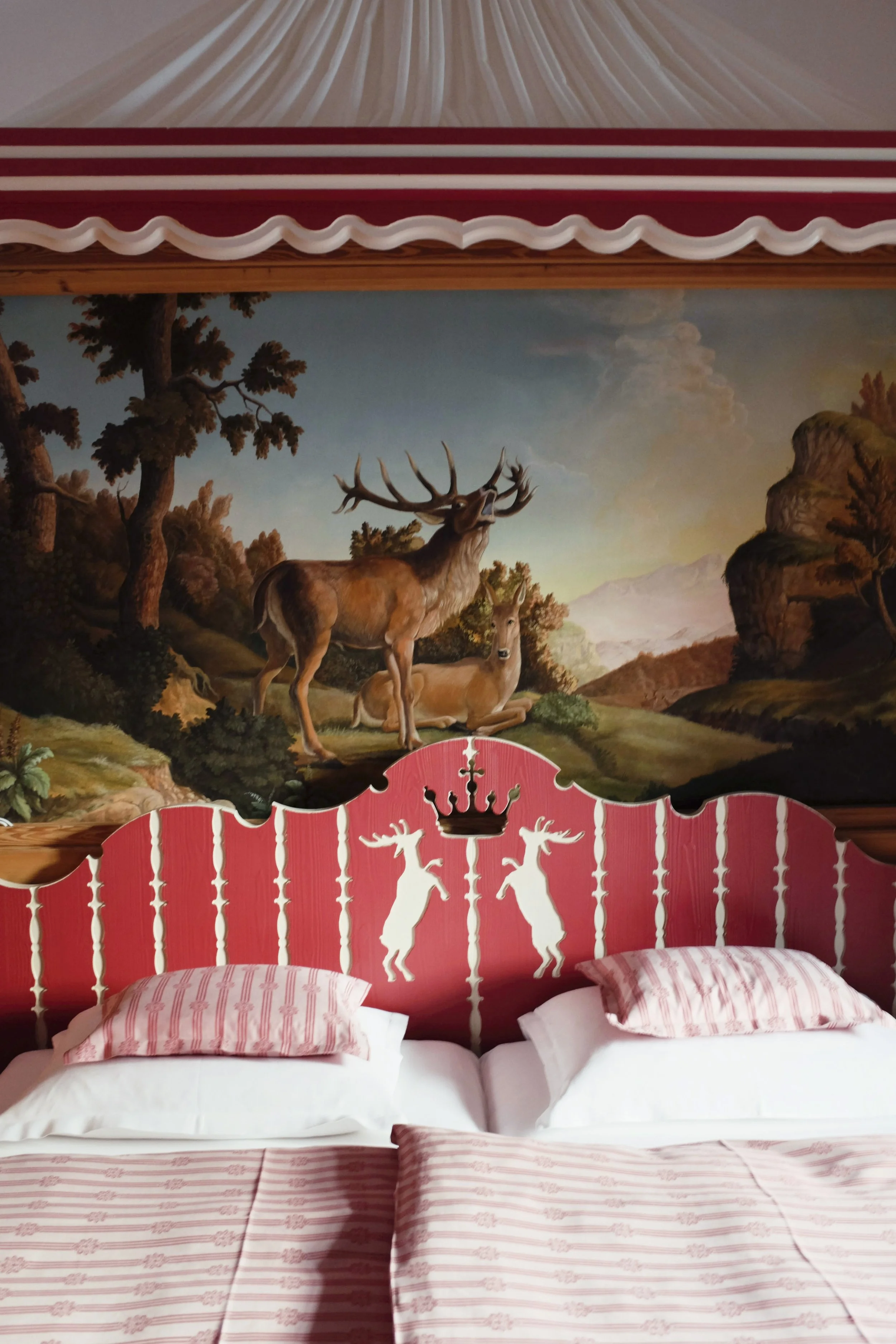 A bedroom with a colorful wall mural featuring trees and deer in a landscape scene, with a pink and white striped bedspread and pillows with matching pillowcases.