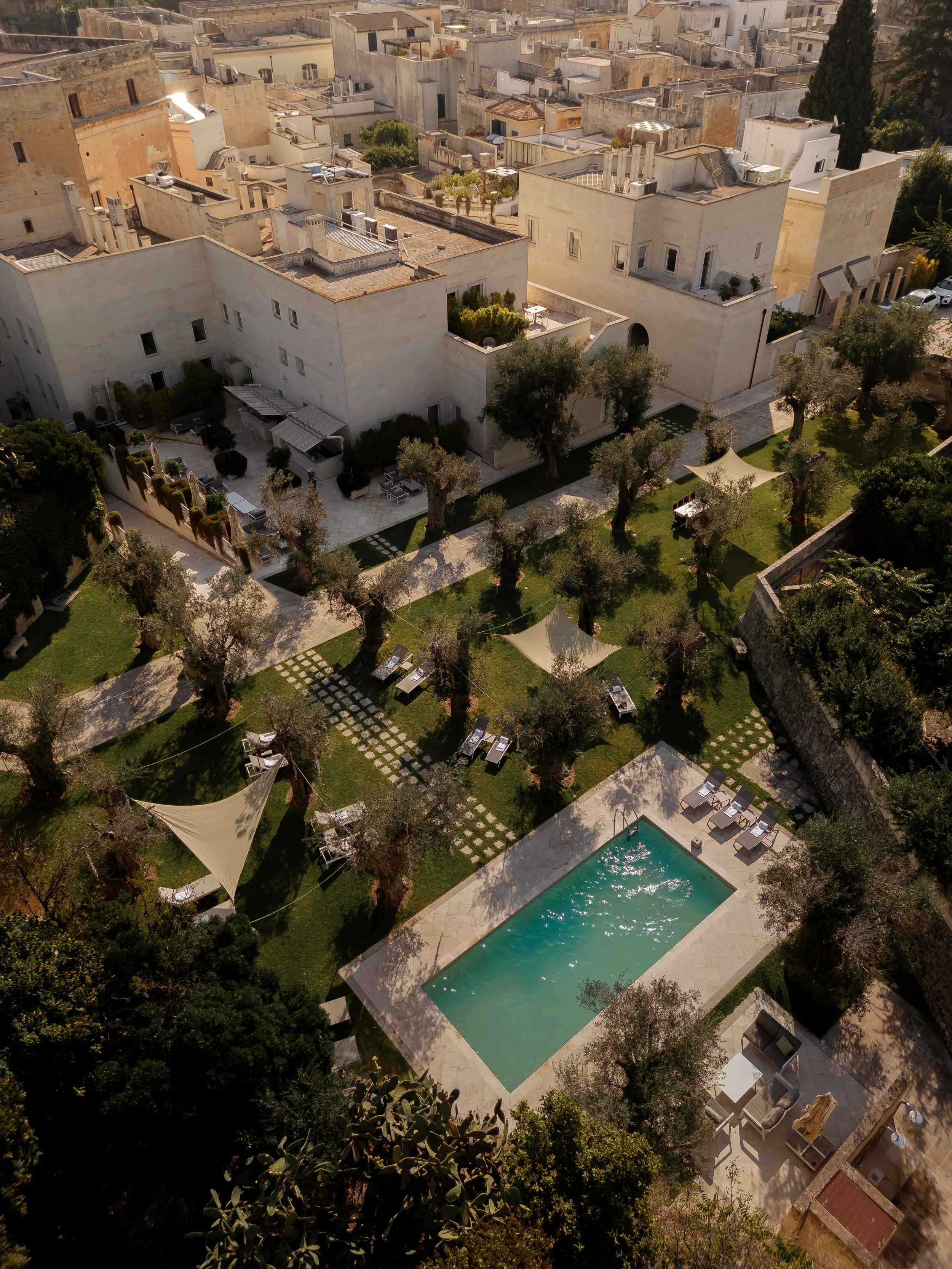 An aerial view of a residential area with modern buildings, a swimming pool, and a garden with trees and outdoor furniture.