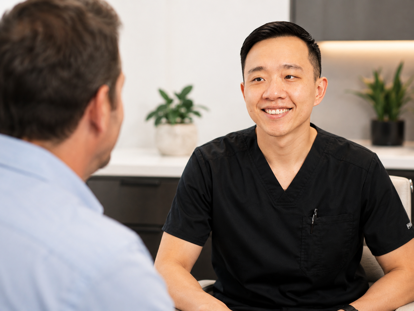 Two men having a conversation inside an office, with two plants in the background.