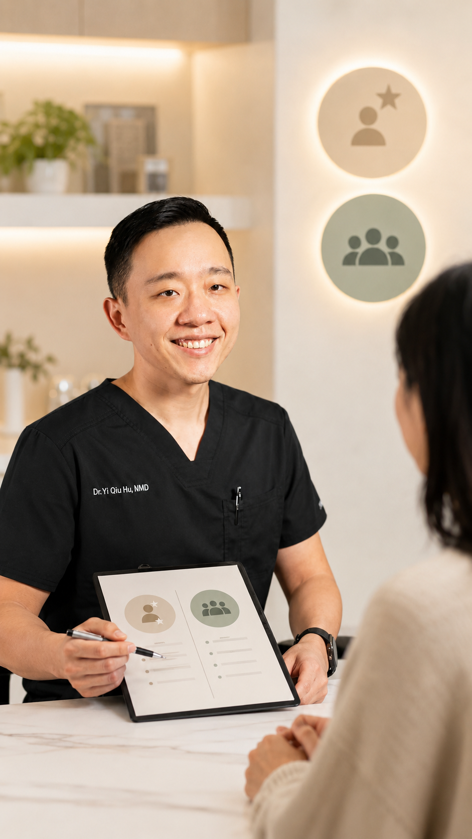 A medical professional, Dr. Yi Qiu Hu, wearing black scrubs, is smiling and showing a chart to a patient during a consultation in a modern, well-lit office.