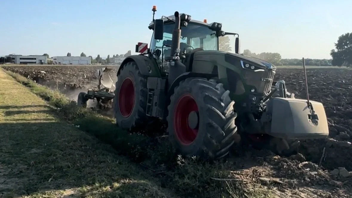 Trattore che lavora su un campo agricolo vicino a un edificio in lontananza.